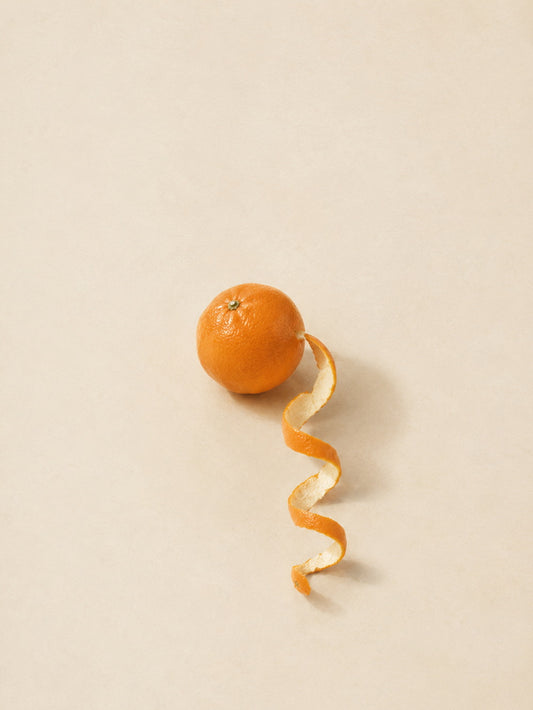 A vibrant orange resting next to its spiral peel on a plain background.